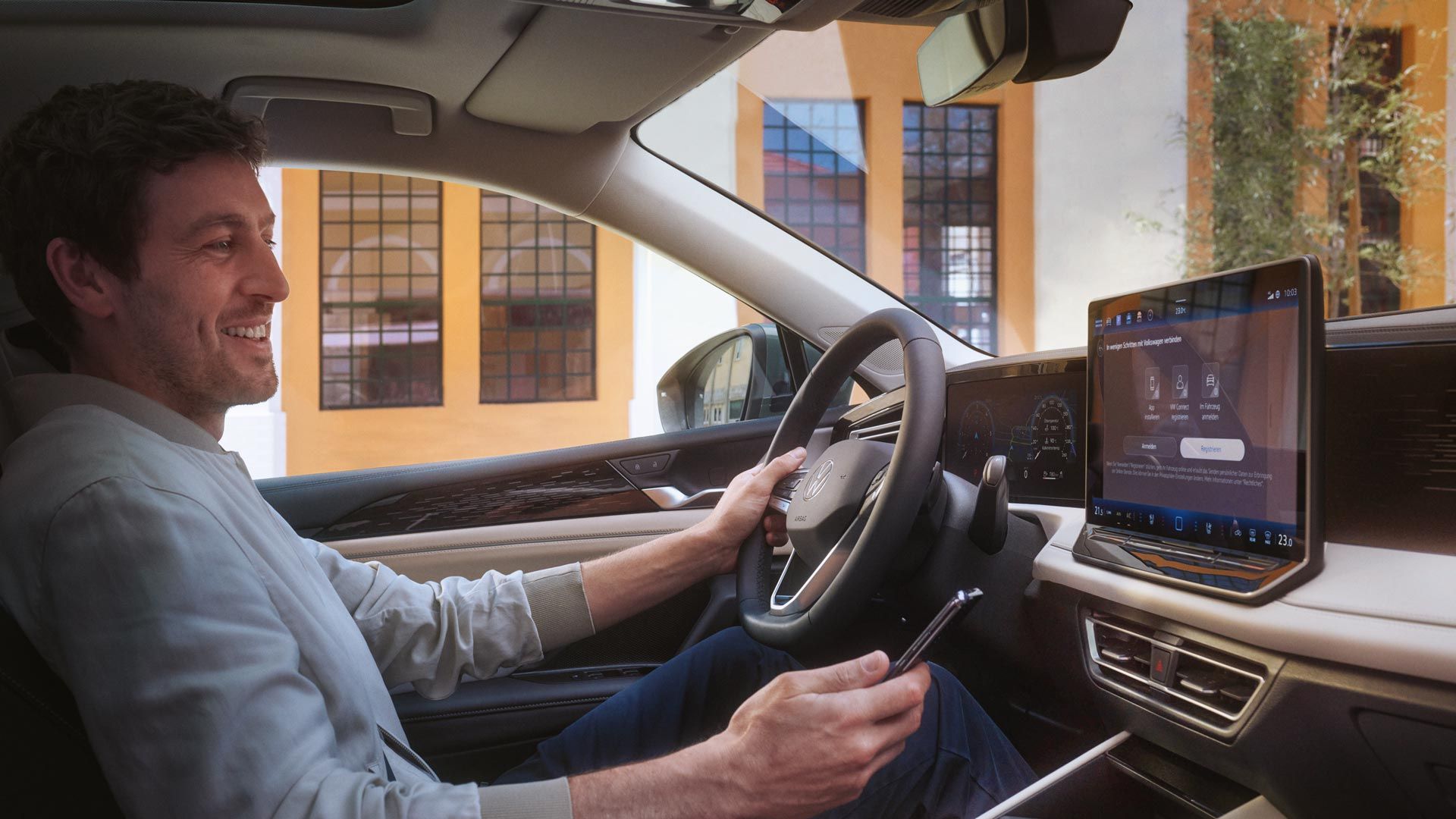 Fotografia do interior de um VW Tiguan. Um homem sentado no banco do condutor utiliza o seu smartphone para controlar a aplicação VW Connect Plus opcional.