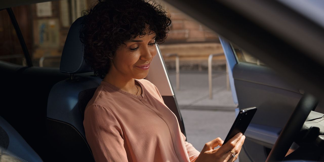 Uma mulher sorridente olha para o telemóvel no banco do condutor de um VW T-Cross estacionado.