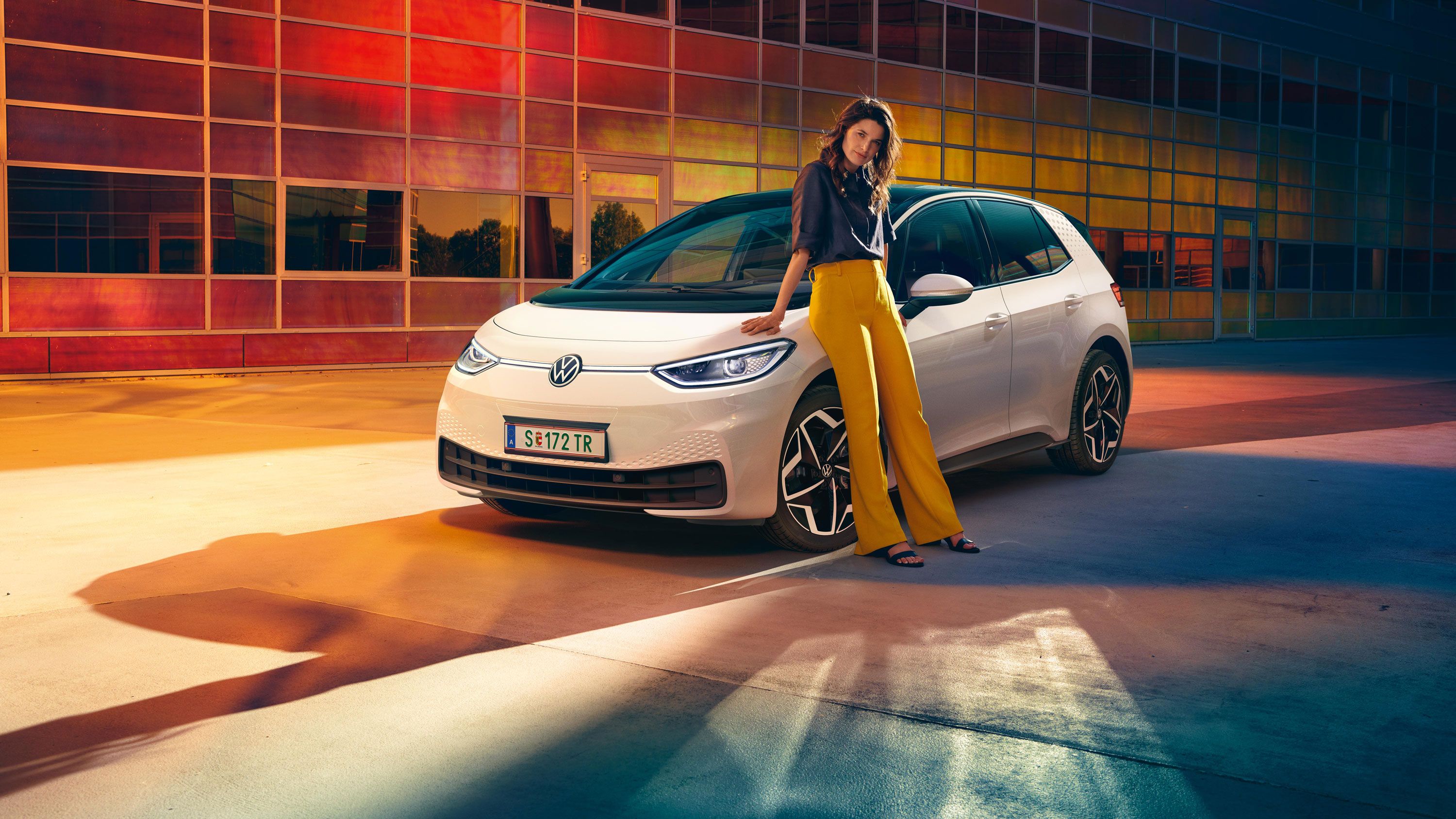 VW ID.3 em branco, vista frontal com faróis e jantes opcionais Andoya, uma mulher está encostada ao carro.