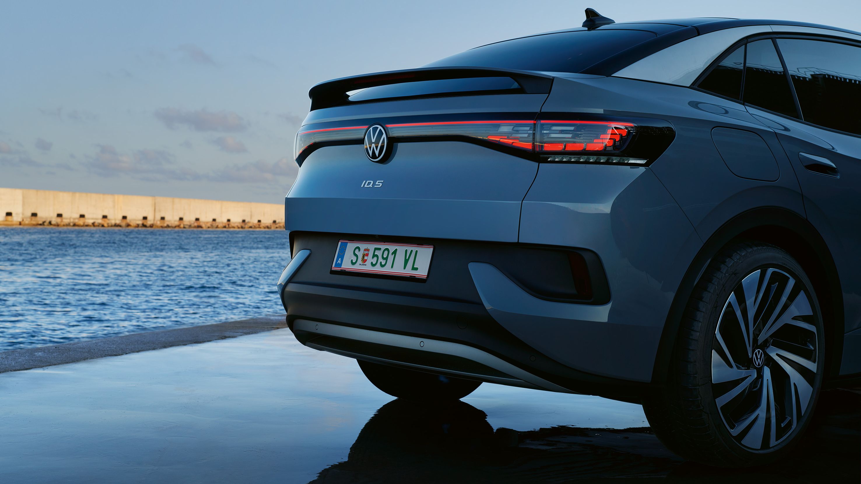 Traseira de um VW ID.5 parado, ambiente de fim de tarde junto ao mar, luzes LED traseiras acesas
