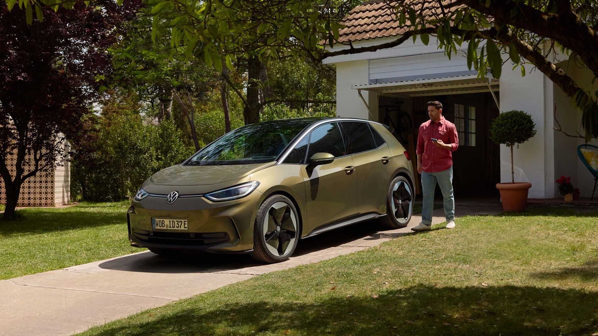 Homem em pé ao lado do Volkswagen ID.3 estacionado em frente a uma casa, rodeada de árvores e vegetação.