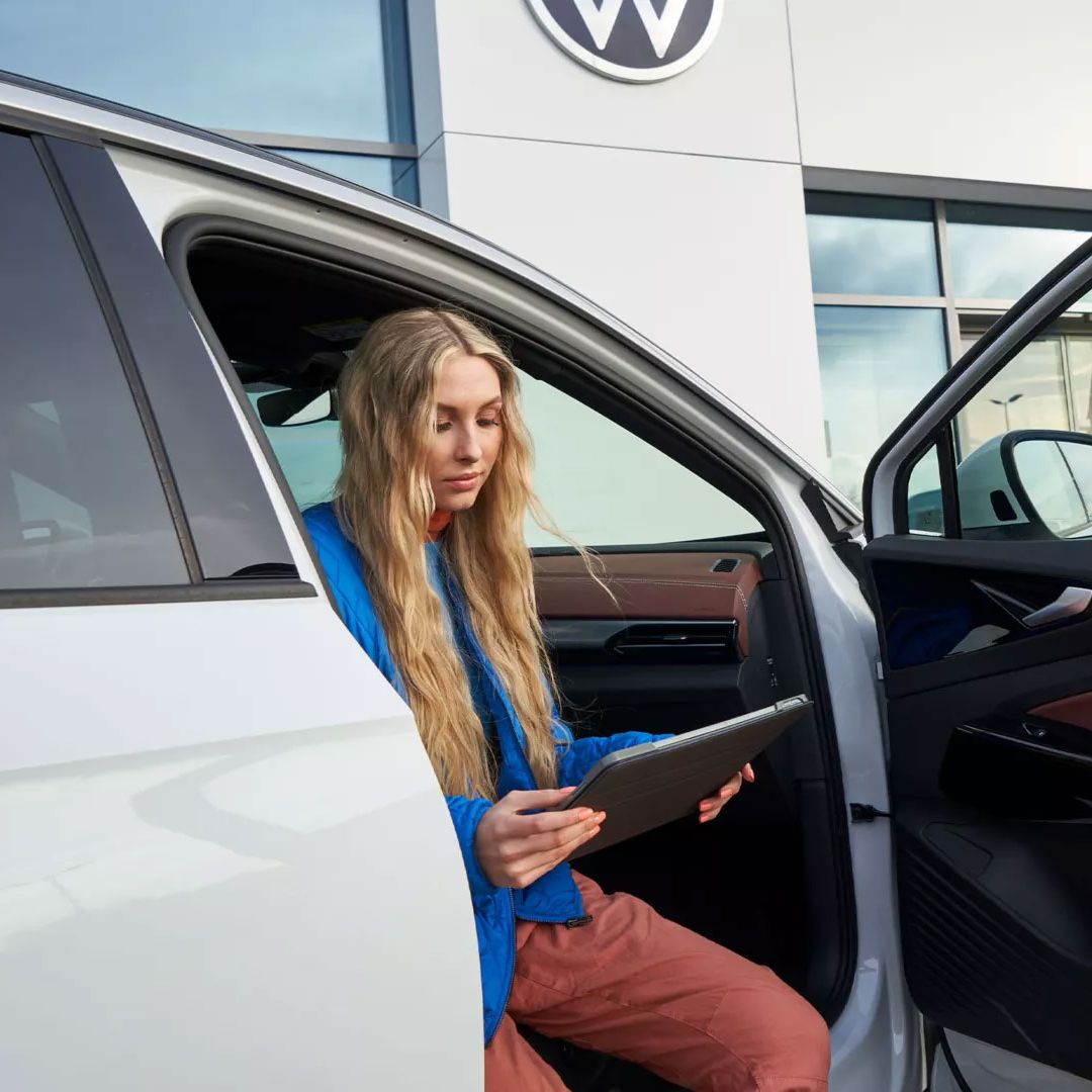 Eine Frau sitzt bei geöffneter Fahrzeugtüre in einem VW ID.