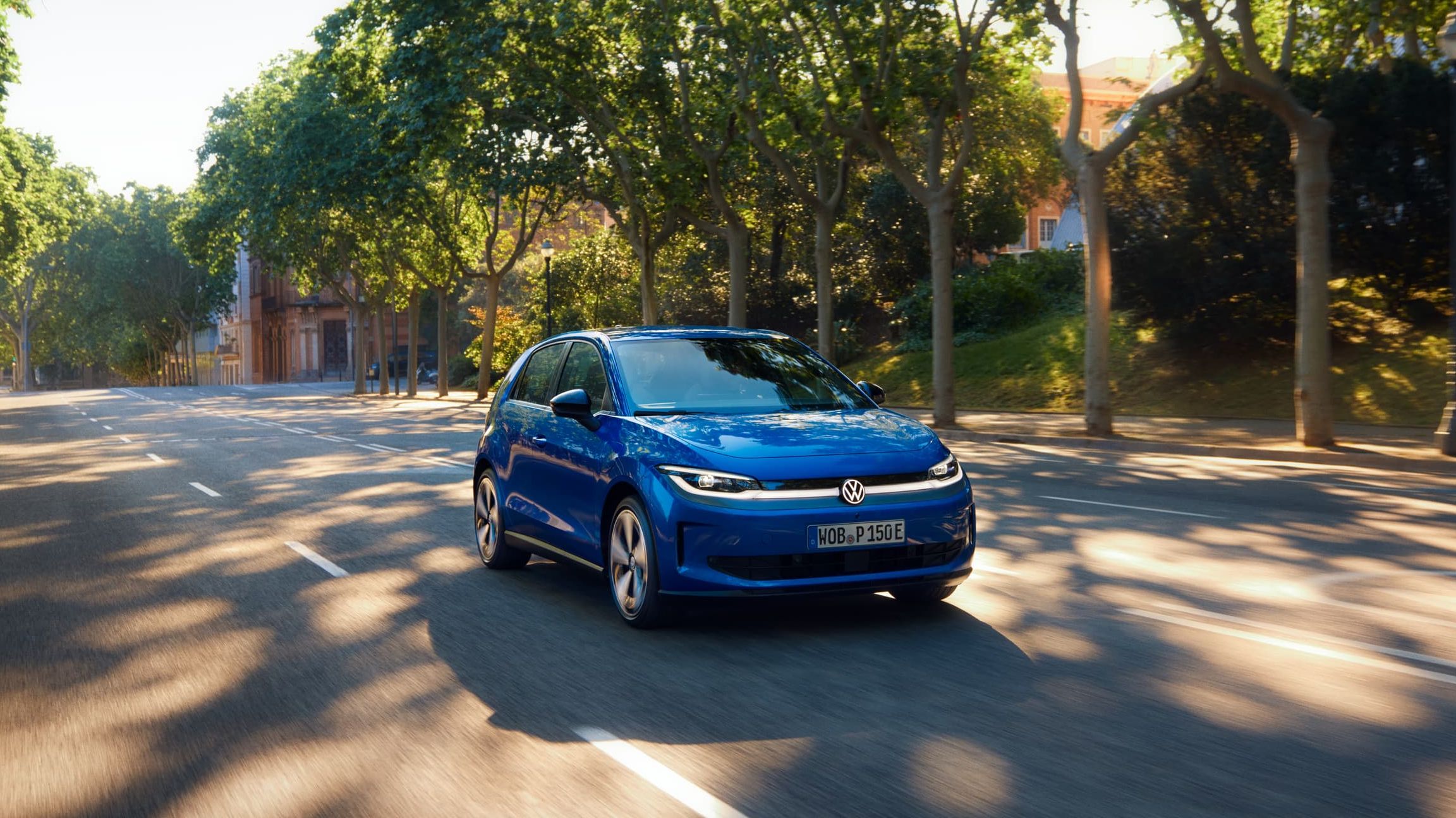 Um VW ID. Polo circula por uma estrada larga, sob a sombra de uma rua arborizada.