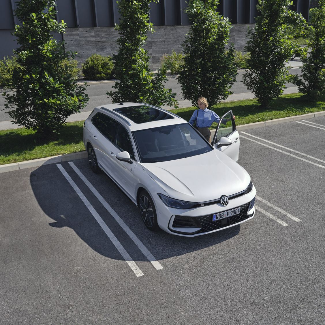 Fotografia de cima de um VW Passat branco num parque de estacionamento, uma mulher entra no lado do condutor.