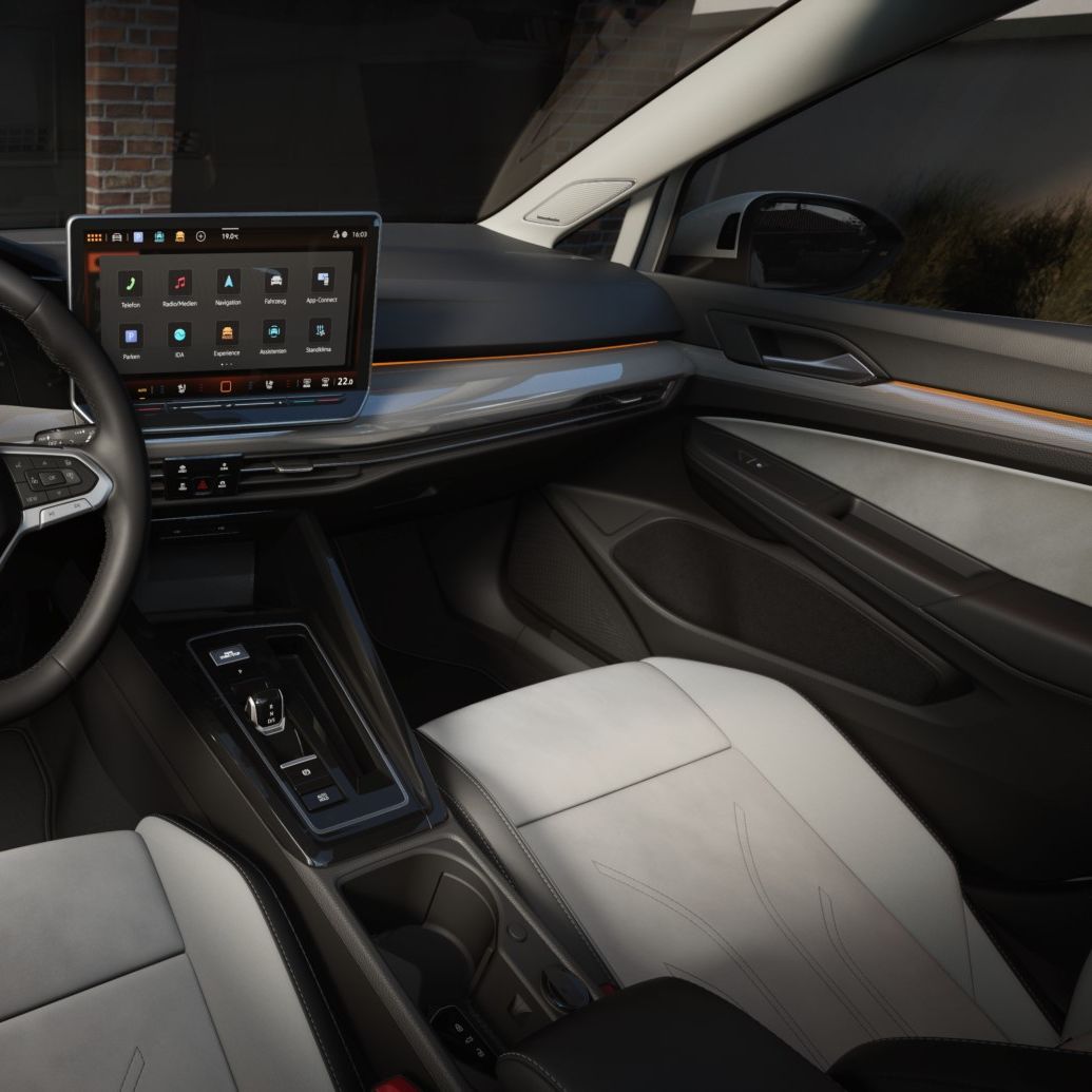 Blick auf den Innenraum des VW Golf Estate. Bei geöffneter Beifahrertür legt eine Frau Kopfhörer und ein Tablet in den Wagen hinein.
