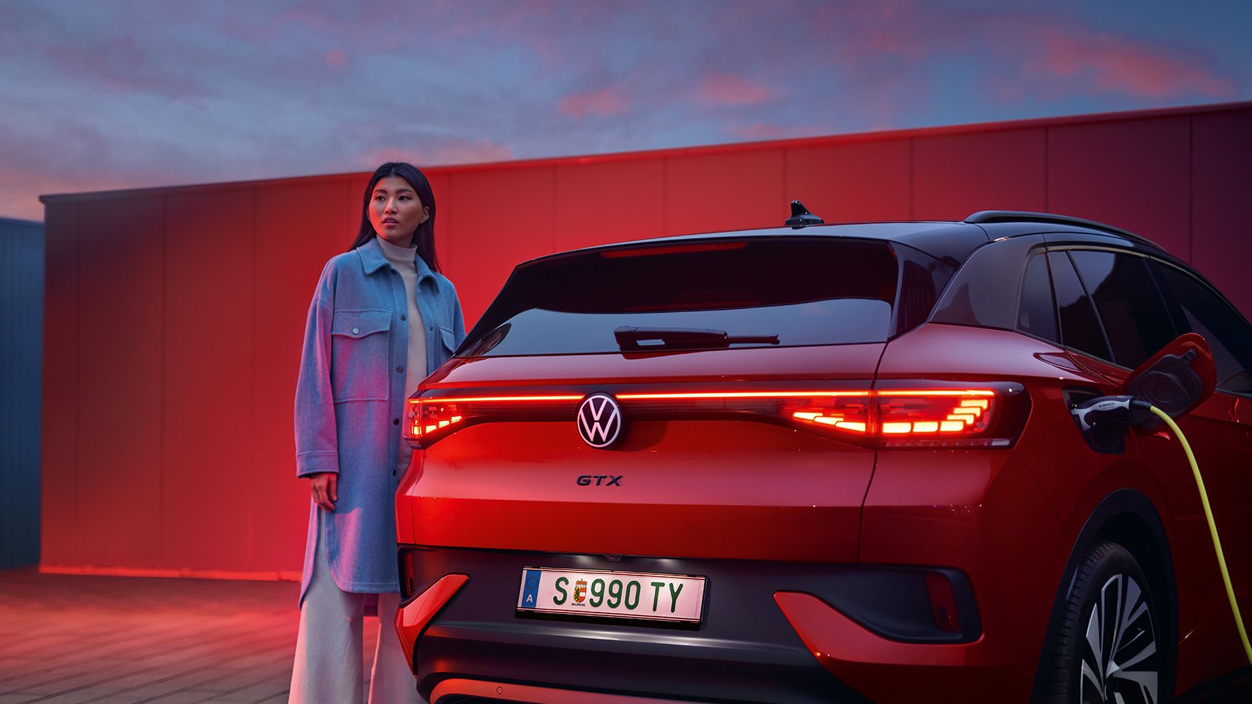 Seitenansicht des VW Tiguan eHybrid in Weiß, welcher am Straßenrand lädt. Junger Mann steigt aus Fahrerseite aus.