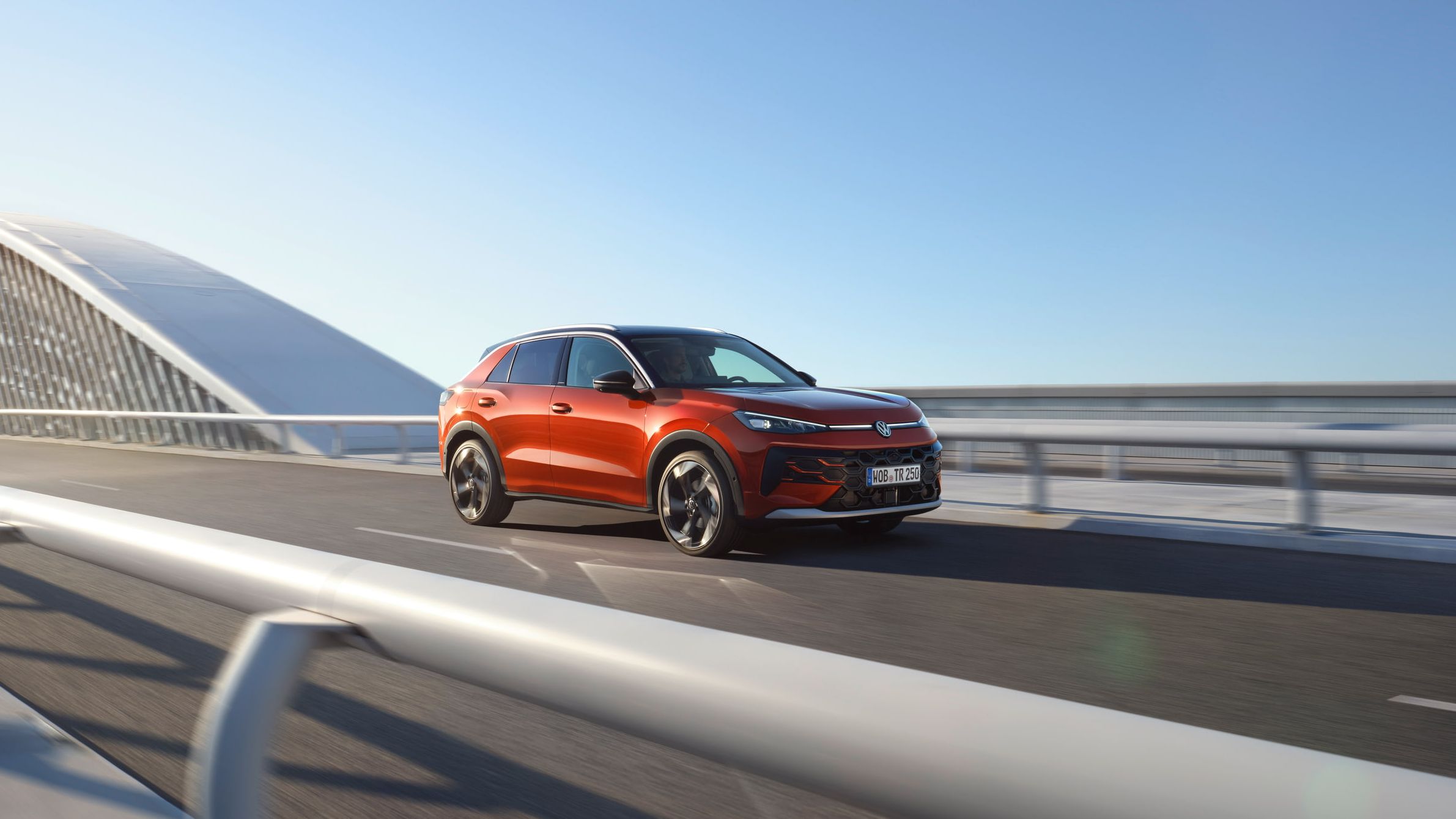 Um VW T-Roc Style vermelho circula numa ponte moderna.