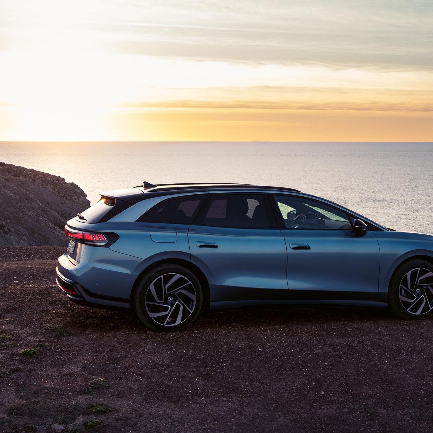Um VW ID.7 Tourer no topo de uma falésia ao pôr do sol com o mar por trás.