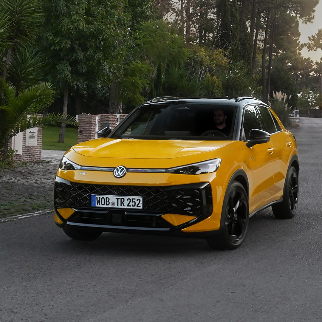 Um VW T-Roc R-Line amarelo percorre uma estrada numa zona arborizada.