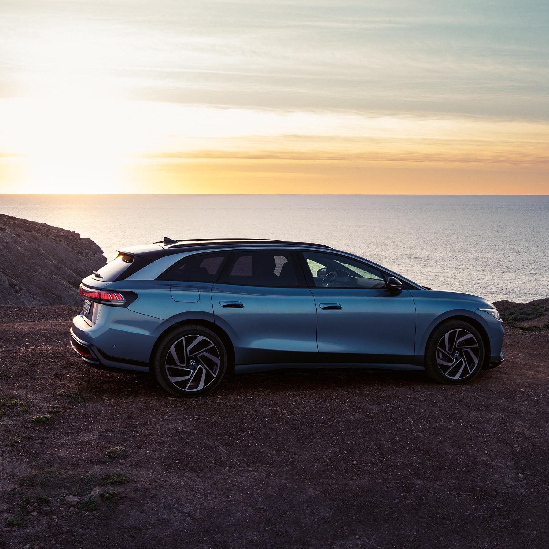 Um VW ID.7 Tourer no topo de uma falésia ao pôr do sol com o mar por trás.