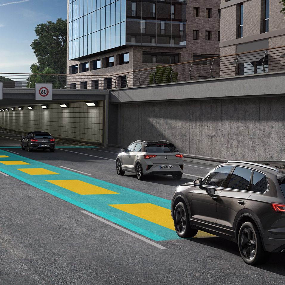 Um VW Touareg cinzento escuro segue ao longo de uma estrada em direção a um túnel sobre uma linha verde e amarela.