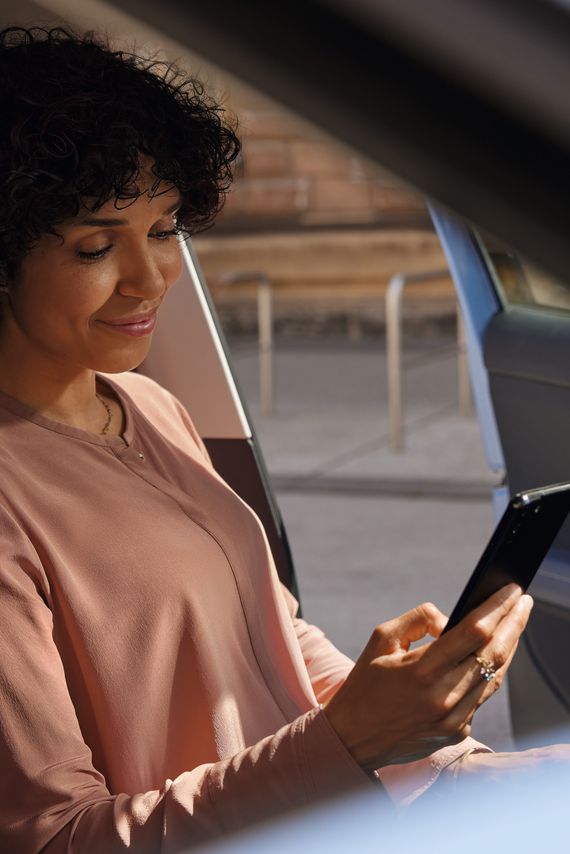 Uma mulher sorridente olha para o telemóvel no banco do condutor de um VW T-Cross estacionado.