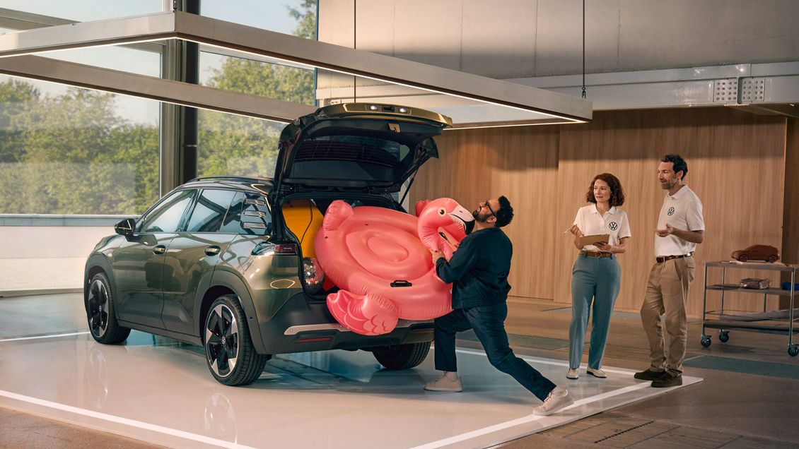 Um homem empurra um flamingo insuflável para dentro da bagageira aberta do VW ID. Cross. Duas pessoas estão ao seu lado e divertem-se a olhar para ele.