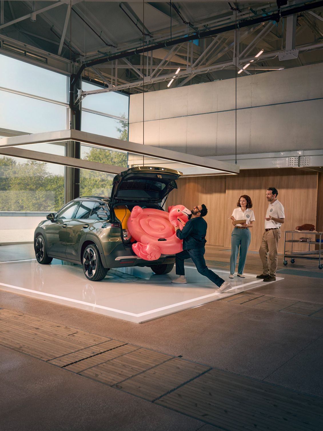 Um homem empurra um flamingo insuflável para dentro da bagageira aberta do VW ID. Cross. Duas pessoas estão ao seu lado e divertem-se a olhar para ele.