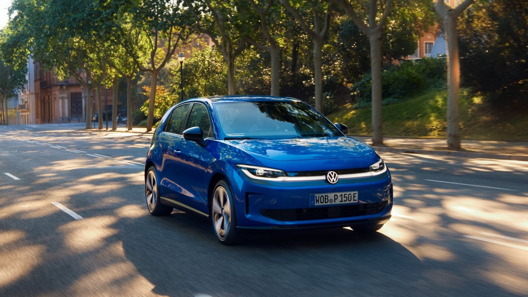 Um VW ID. Polo circula por uma estrada larga, sob a sombra de uma rua arborizada.