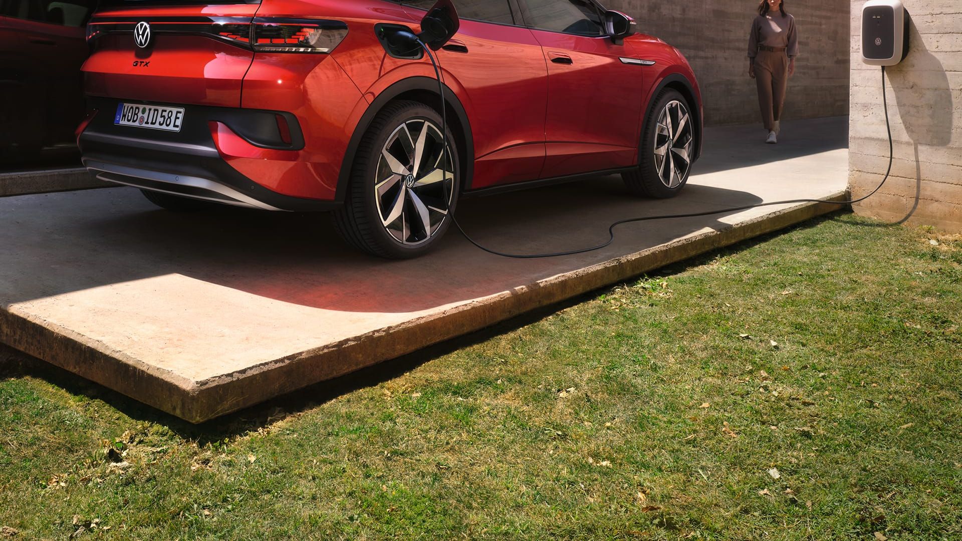 VW ID.5 GTX em vermelho em frente a uma casa moderna e a carregar num ID. Charger, um homem dirige-se para o carro