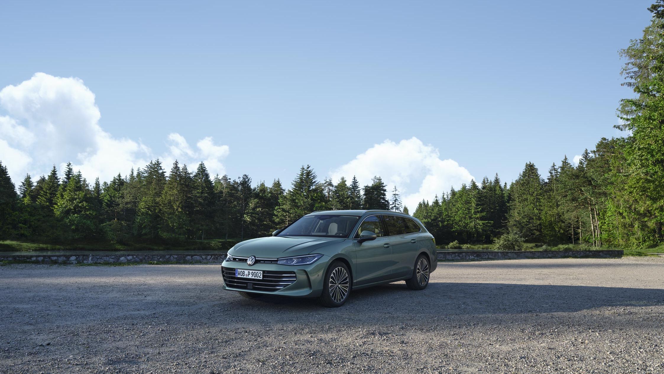 VW Passat verde-azulado sobre uma superfície de gravilha, a área confina com um pinhal.