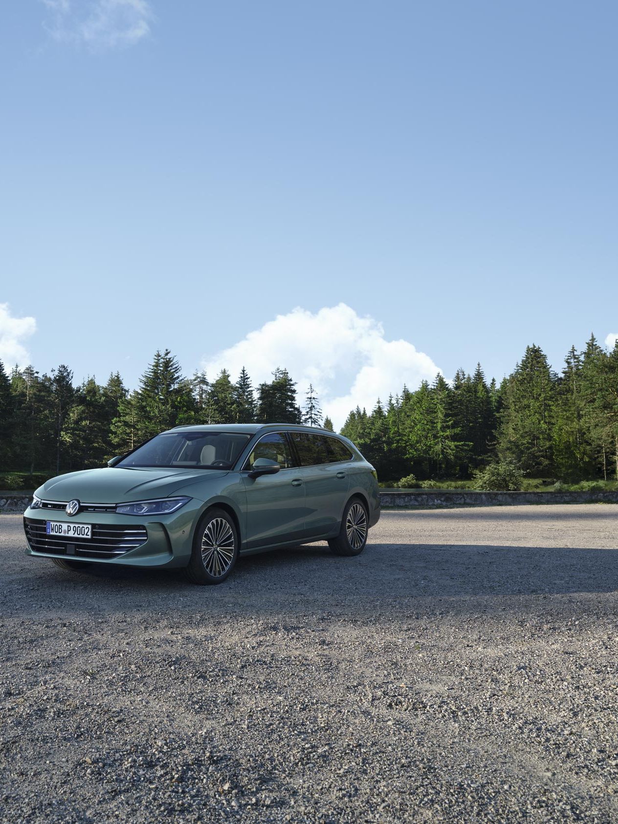 VW Passat verde-azulado sobre uma superfície de gravilha, a área confina com um pinhal.