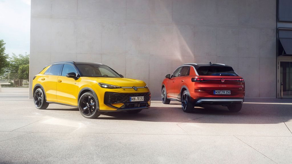  Um VW T-Roc R-Line amarelo e um VW T-Roc Style vermelho estão lado a lado em frente a um edifício moderno.