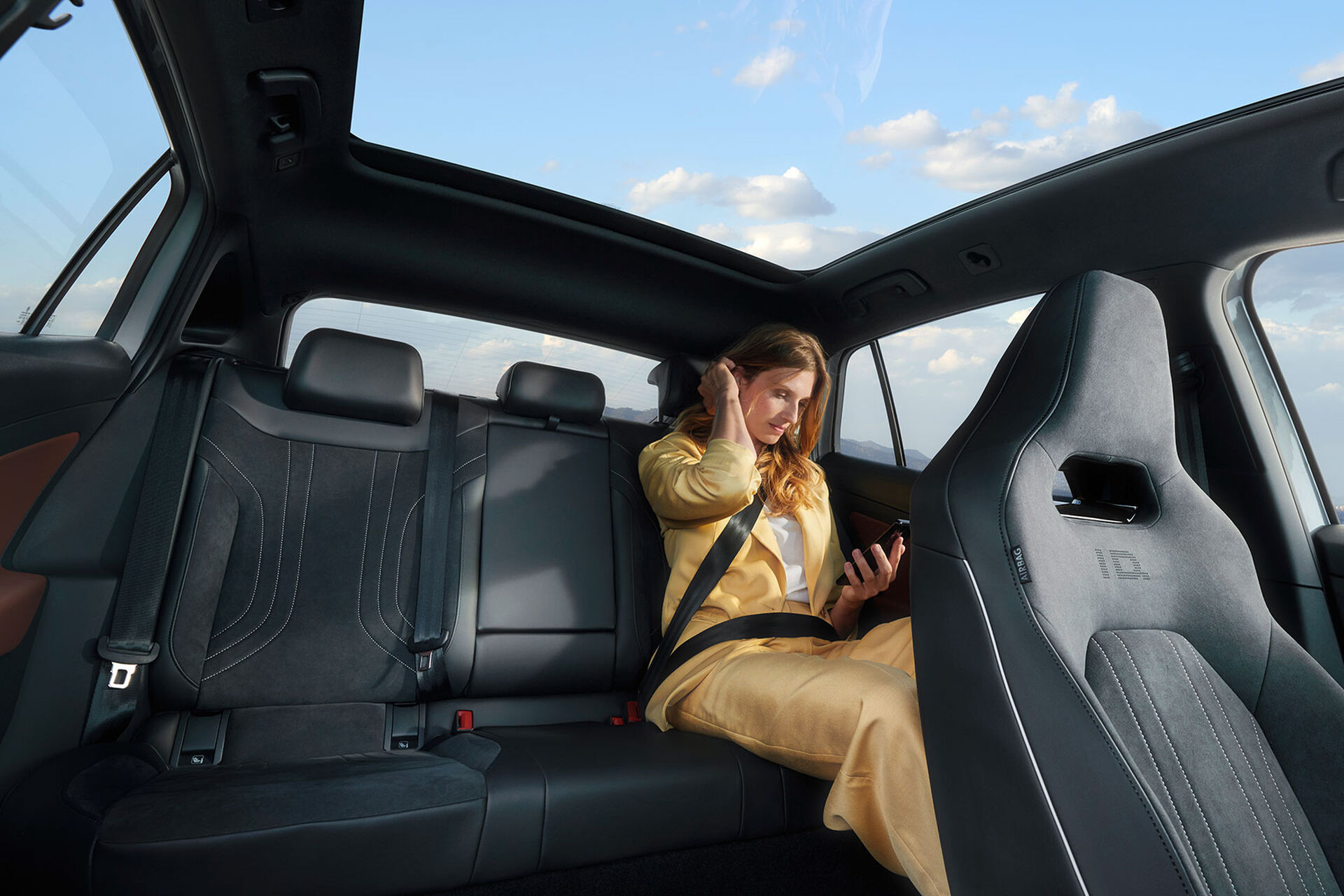 Vista interior de um VW ID.5, vista de frente para o banco traseiro, onde está sentada uma mulher a ler