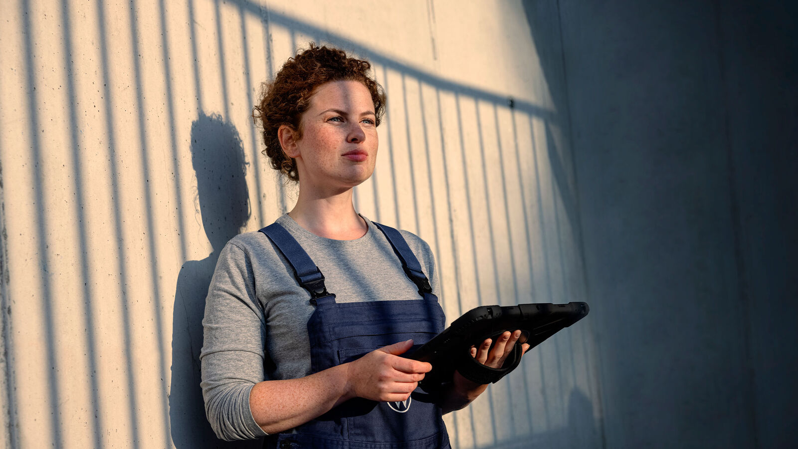 Eine Servicemitarbeiterin lehnt mit einem Tablet in der Hand an einer Wand