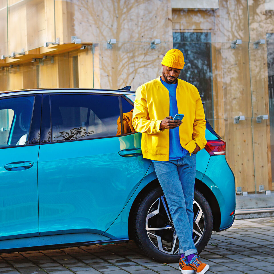 Ein Mann in einer gelben Jacke lehnt an seinem VW ID