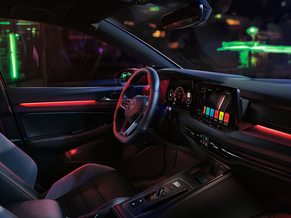 Interior do VW Golf GTI, cockpit com iluminação ambiente vermelha, com foco no banco do condutor