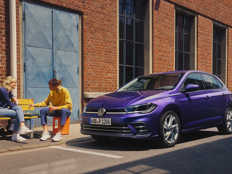 Volkswagen Polo Style com pacote Black Style opcional estacionado junto a uma velha fábrica. Ao lado, um casal joga xadrez num banco. 