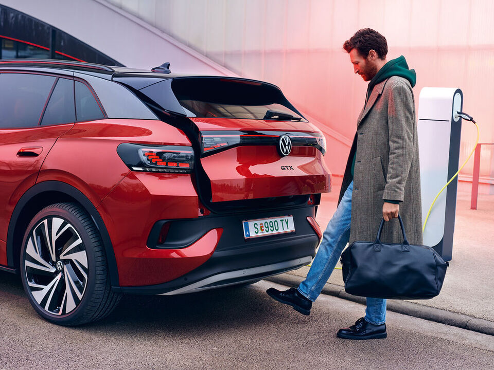 VW ID.4 GTX em vermelho, vista traseira da abertura da bagageira através de sensor, um homem com sacos de compras abre o porta-bagagens.