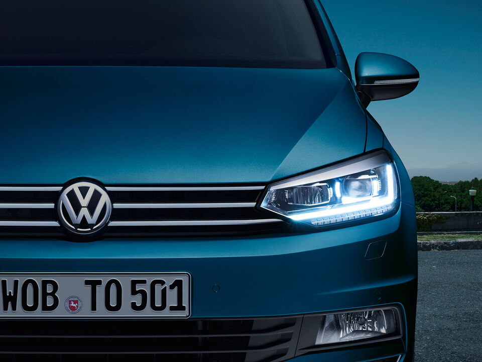 Frente do VW Touran ao anoitecer com faróis LED; luzes de circulação diurna ligadas.