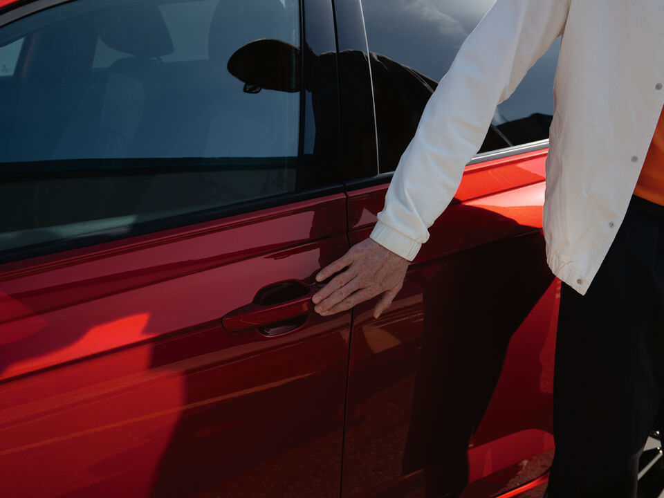 Homem agarra com a mão a maçaneta de um VW Taigo vermelho