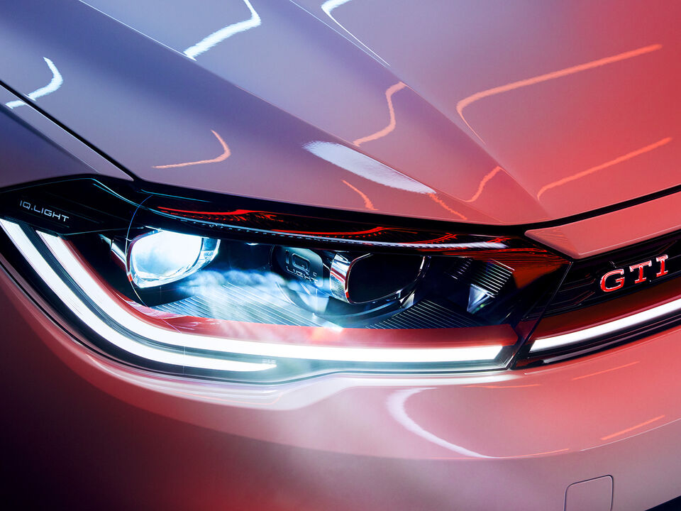 Pormenor dos faróis LED Matrix na dianteira de um VW Polo GTI branco, faixa decorativa vermelha e emblema GTI.