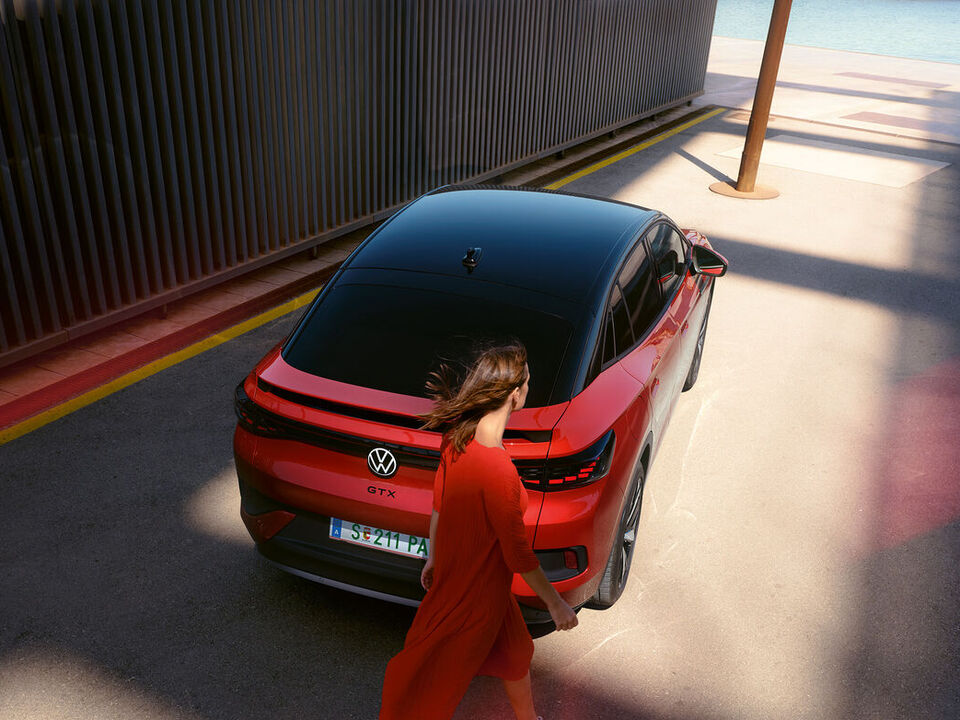 VW ID.5 GTX vermelho numa estrada secundária. Vista de cima sobre o tejadilho e a traseira. Uma mulher jovem vai a passar.