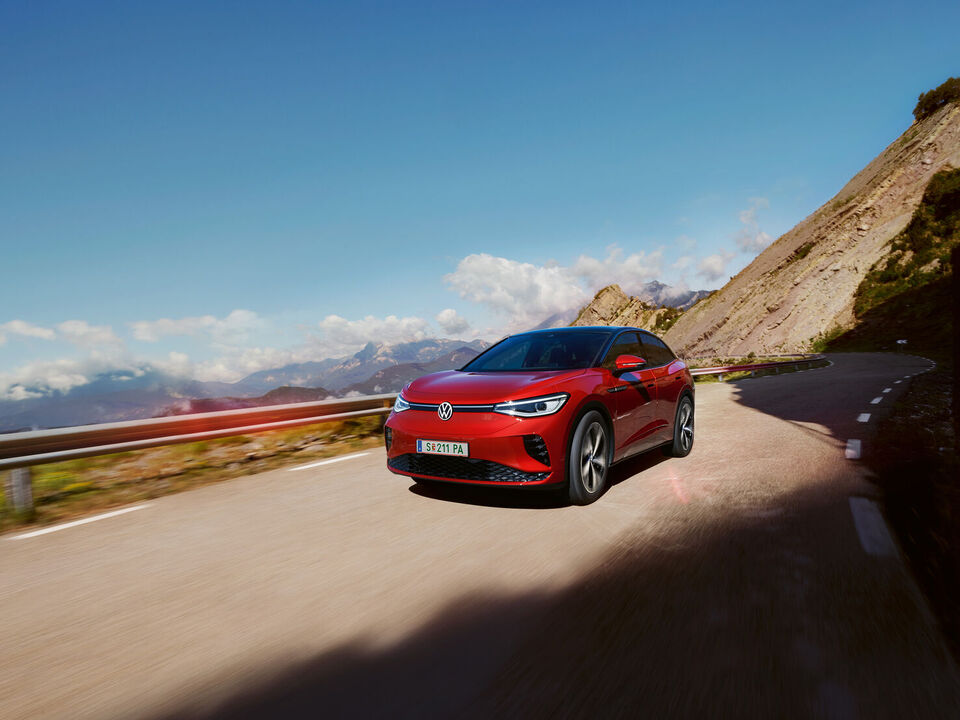 VW ID.5 GTX vermelho desloca-se dinamicamente numa estrada de montanha. Vista da dianteira, rodas e lateral.