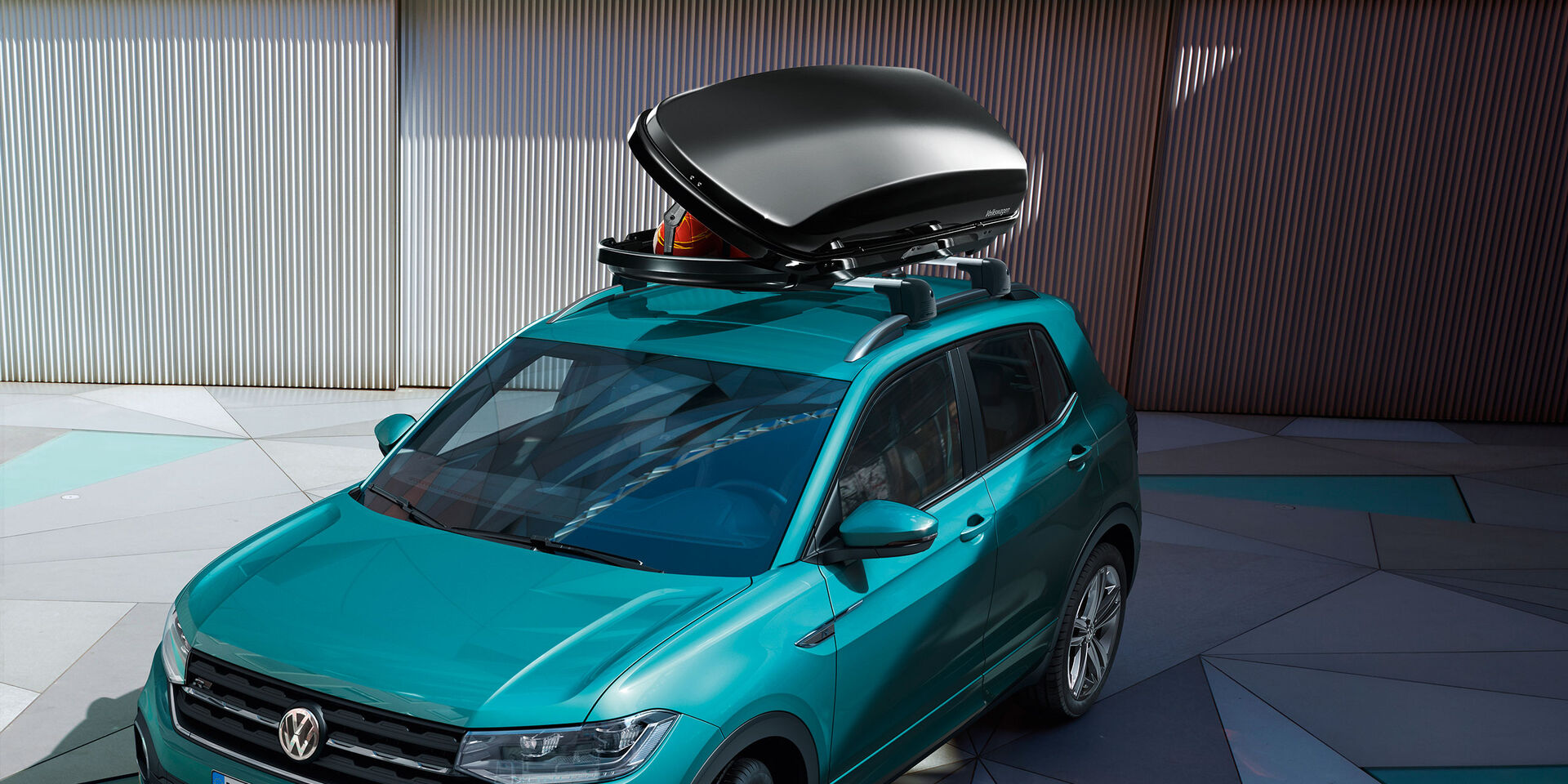 Um VW T-Roc turquesa com uma caixa de acessórios de tejadilho aberta.