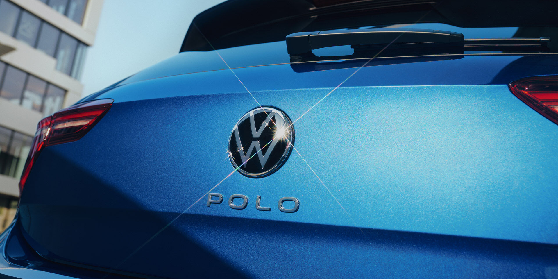 Vista de pormenor do emblema VW e da inscrição "Polo" na porta da bagageira de um Polo azul. 