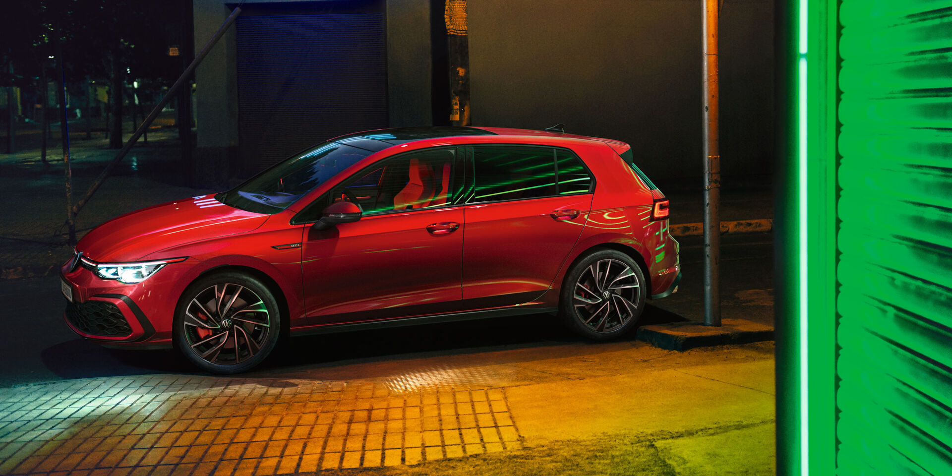  VW Golf GTI, em vermelho, vista lateral, com faróis brilhantes IQ.Light, iluminação ambiente exterior brilhante