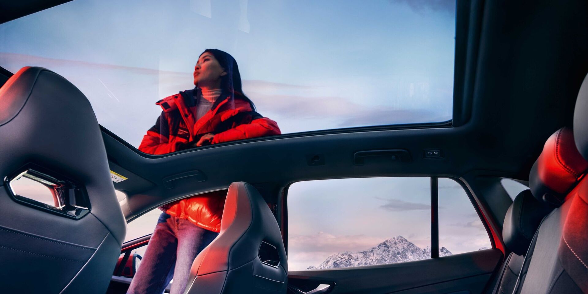 VW ID.4 GTX Vista interior através de teto panorâmico com uma mulher ao lado do SUV desportivo 100% elétrico.