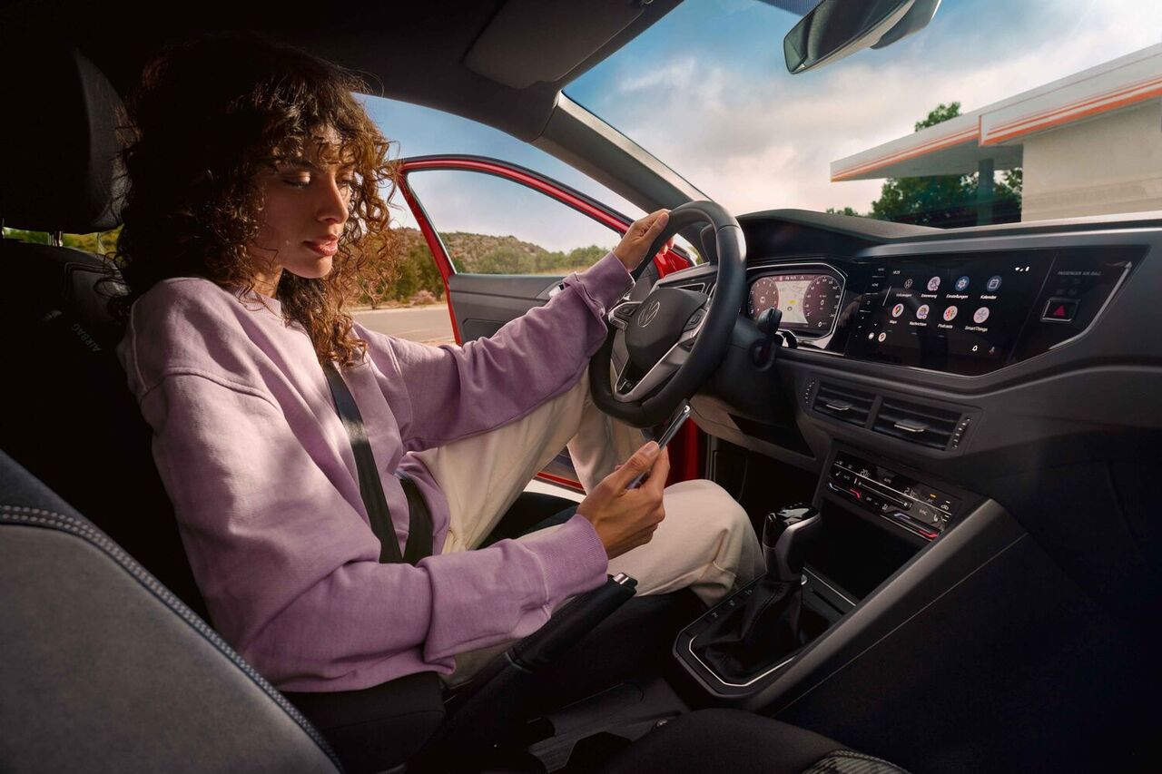 Interior do VW Taigo: Mulher sentada no lugar do condutor, no carro estacionado, a olhar para o smartphone
