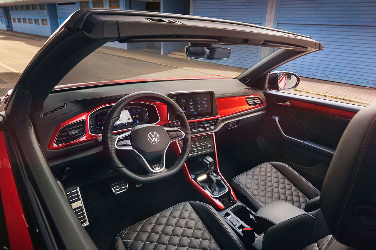Interior do VW T-Roc Cabrio: Vista de cima para o cockpit, através do tejadilho aberto, com elementos decorativos em vermelho e os bancos da frente. 