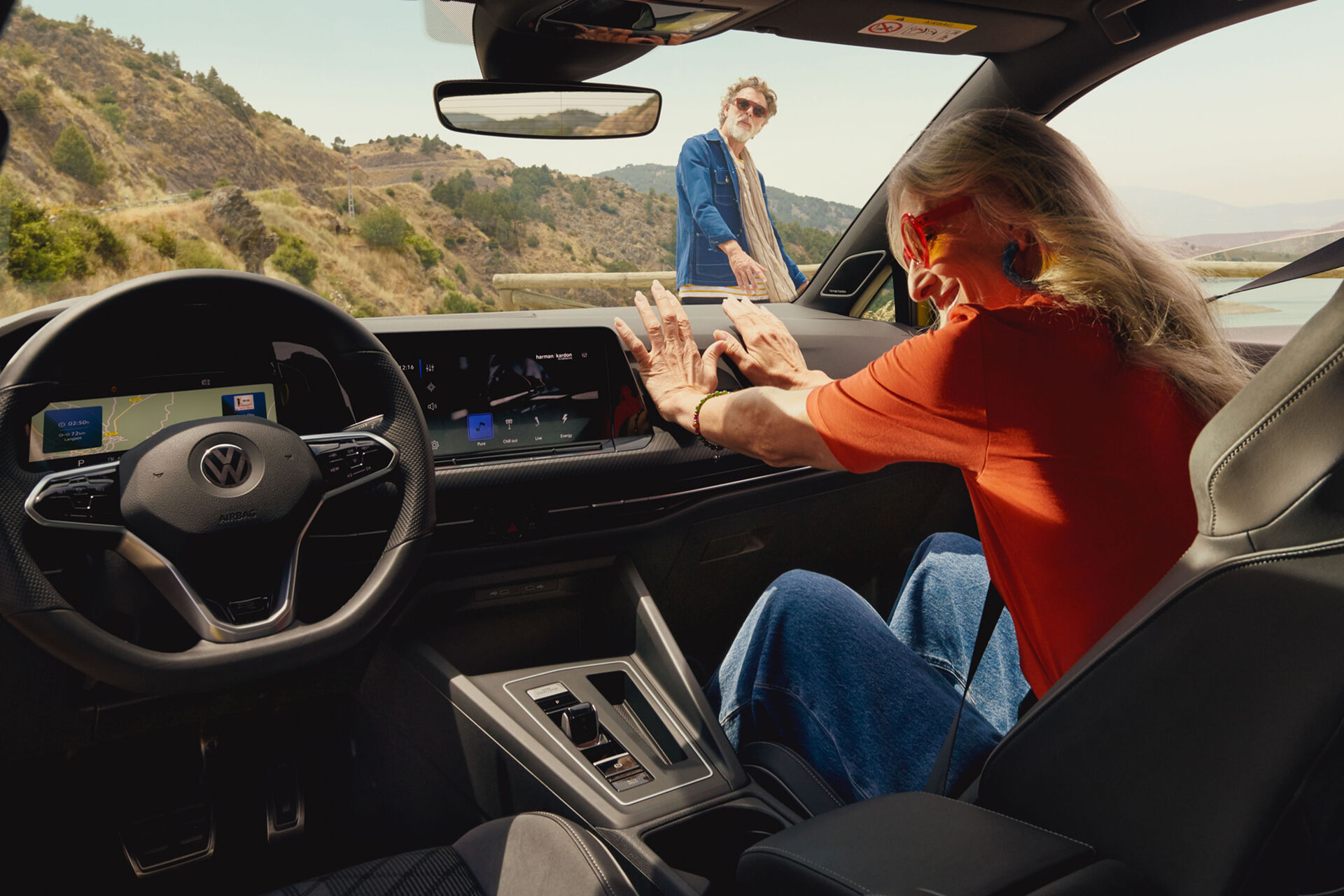 Vista interior do VW Golf com uma mulher sentada no lugar do pendura; está um homem de fora a observar