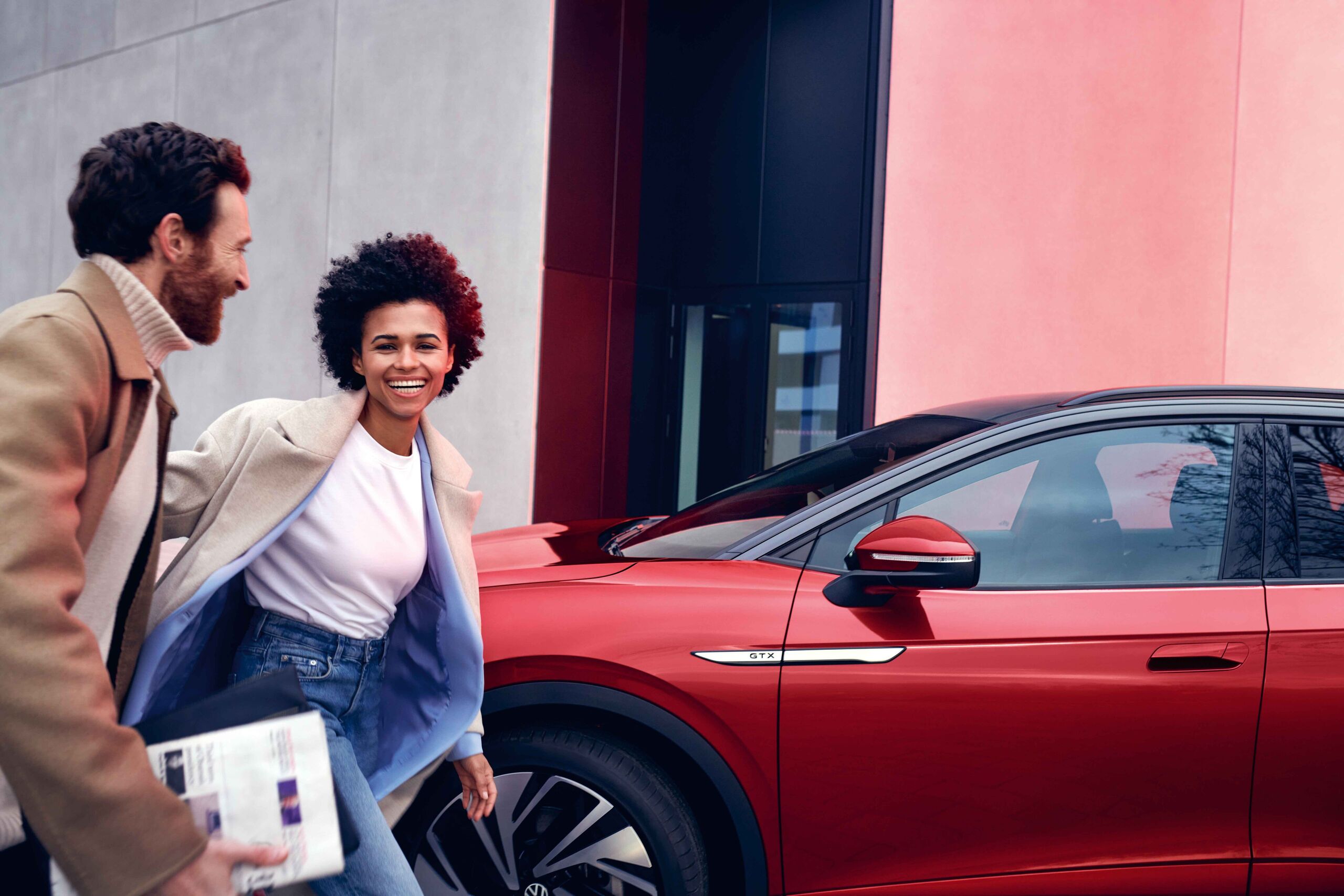 VW ID.4 GTX em vermelho na berma da estrada. Homem e mulher caminham sorridentes.
