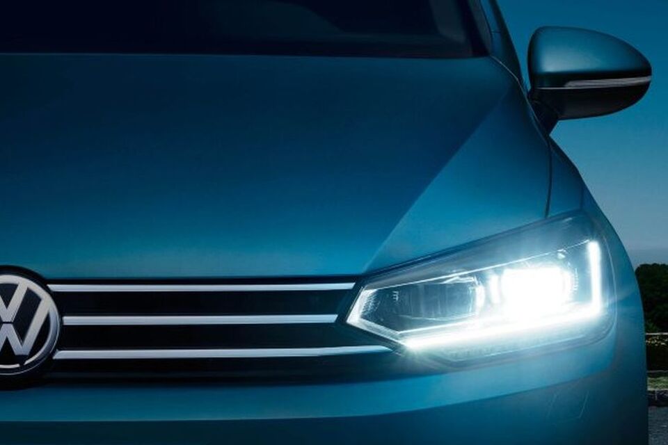 Frente do VW Touran ao anoitecer com faróis LED e luzes de circulação diurna ligadas.