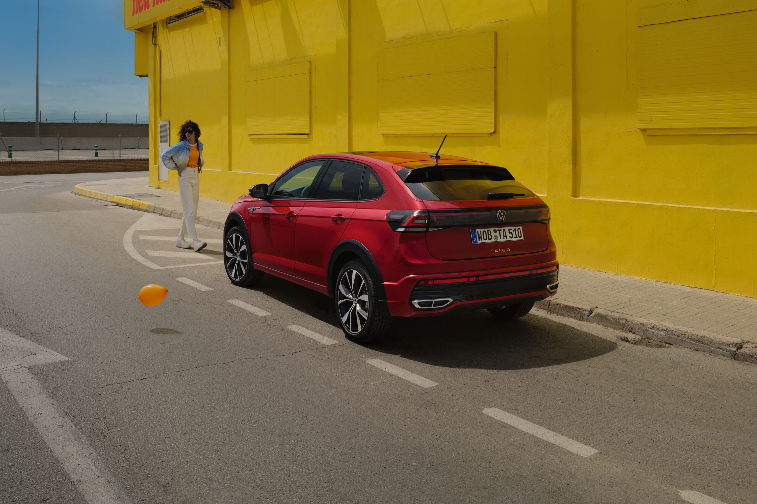 Volkswagen Taigo em vermelho na berma da estrada, em frente a um edifício amarelo, vista traseira