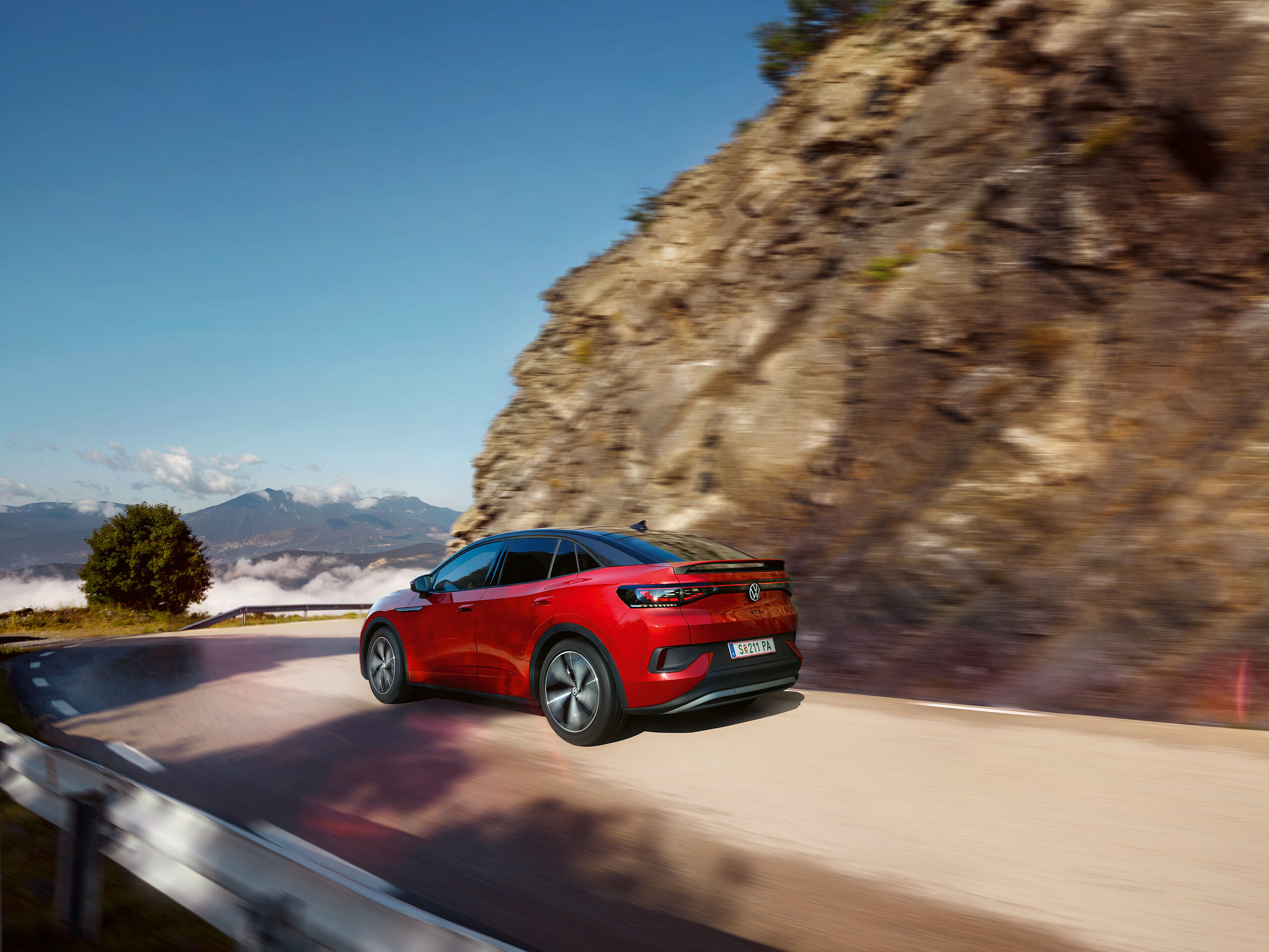VW ID.5 GTX vermelho desloca-se dinamicamente numa estrada de montanha. Vista da lateral, rodas e traseira.