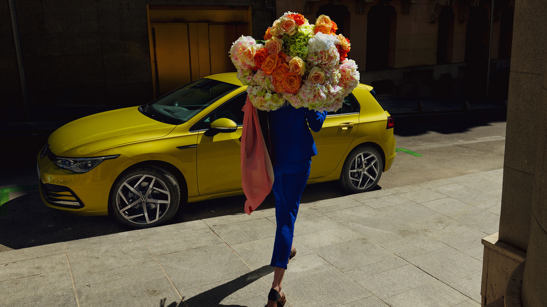 Mulher com um grande ramo de flores caminha em direção ao VW Golf