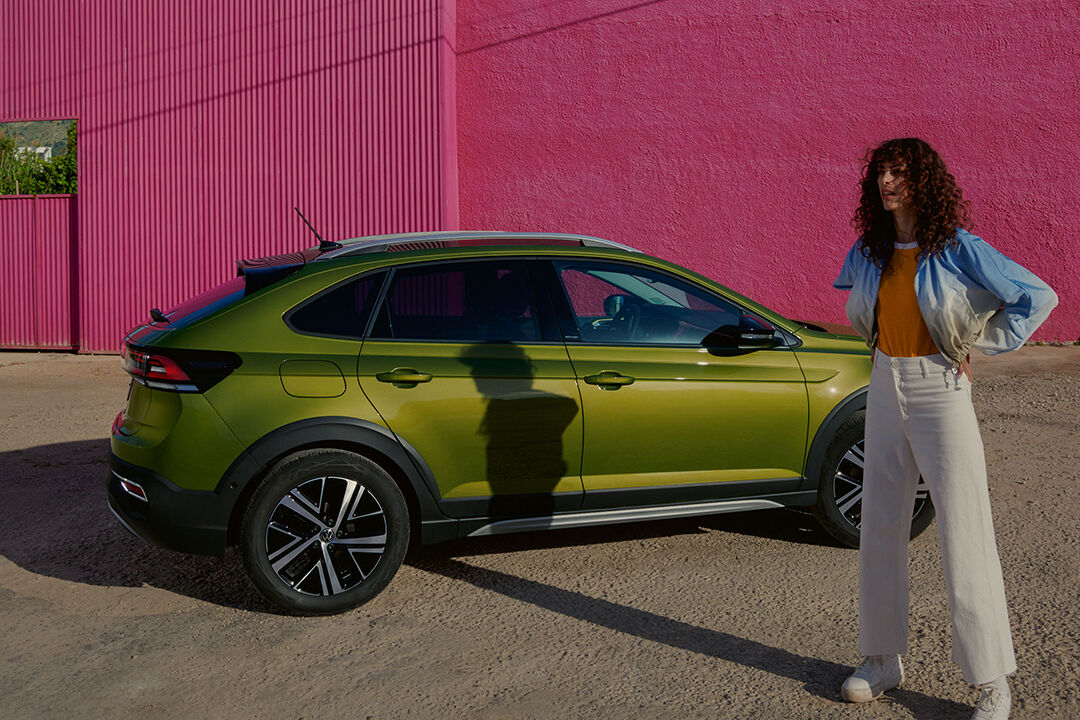 Vista lateral de VW Taigo verde num parque de estacionamento; mulher em pé em frente do automóvel
