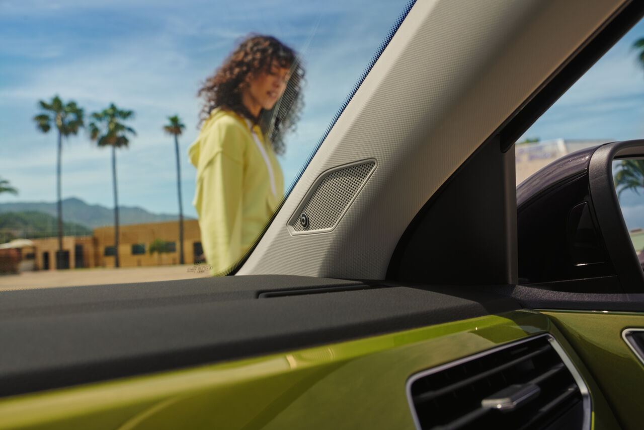 Vista de uma mulher através do pára-brisas do VW Taigo; no cento, altifalantes do sistema de som opcional BeatsAudio™