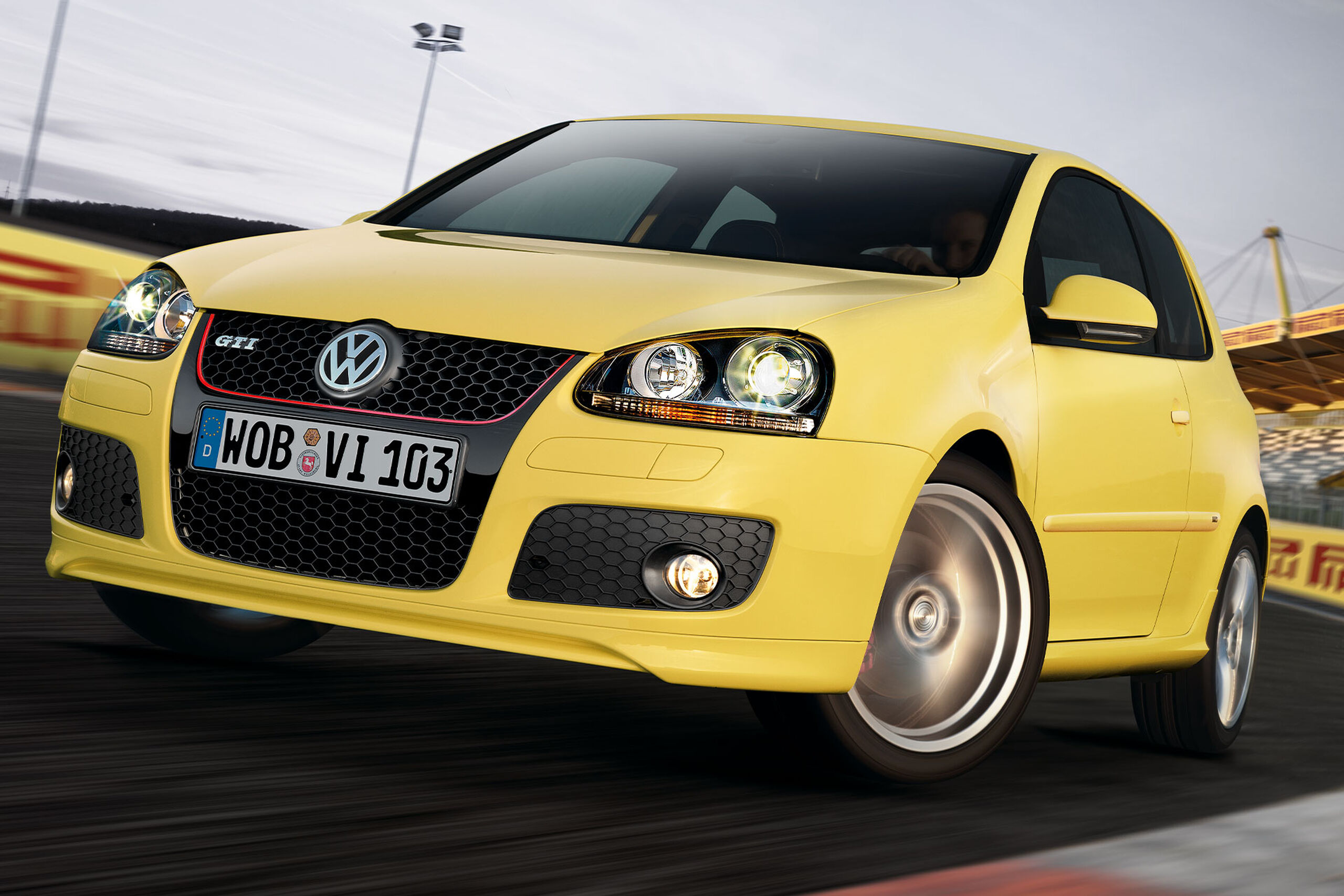 Um Volkswagen Golf 5 GTI amarelo numa pista de corridas com publicidade da Pirelli ao fundo