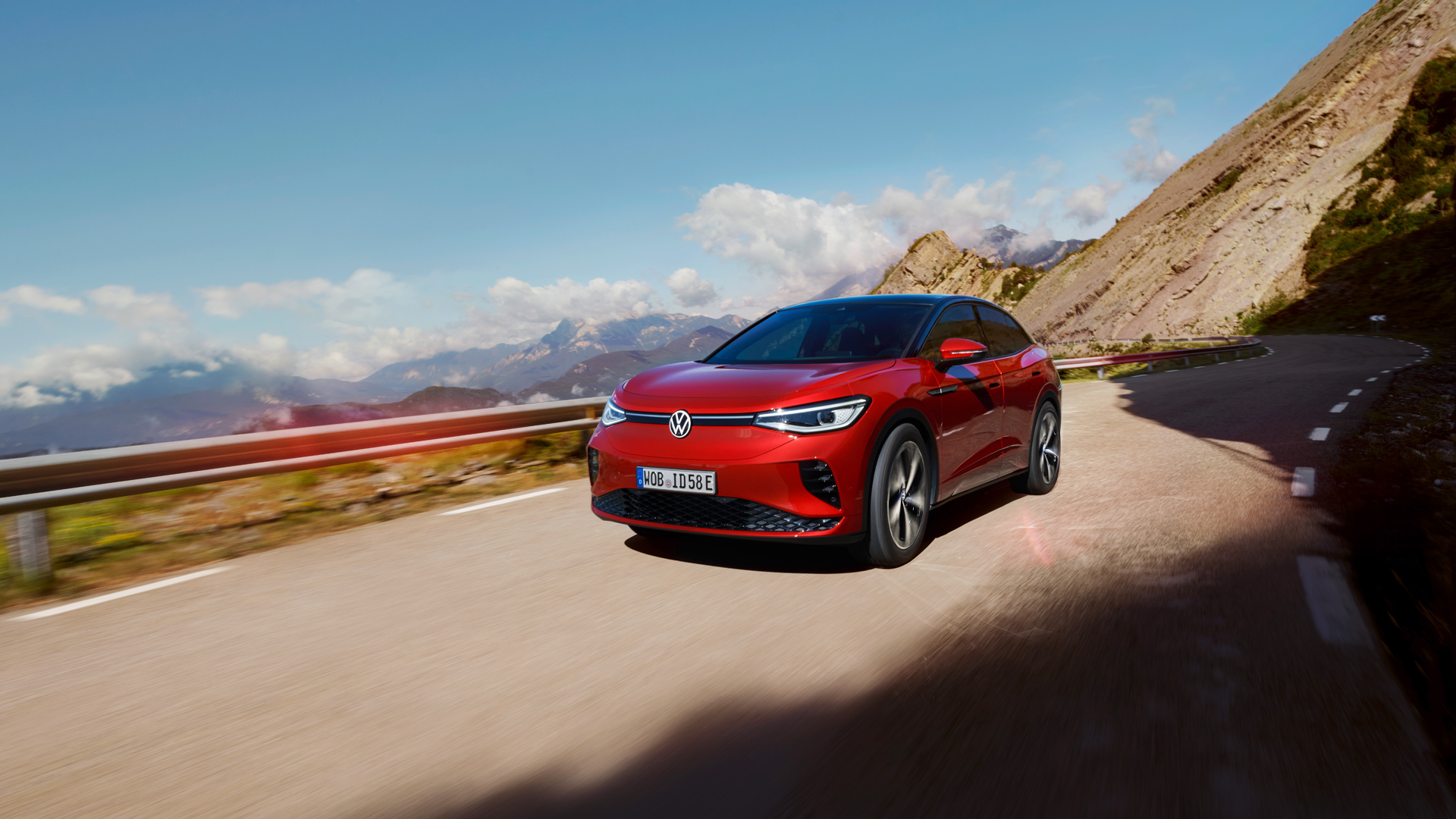 VW ID.5 GTX vermelho desloca-se dinamicamente numa estrada de montanha. Vista da dianteira, rodas e lateral.